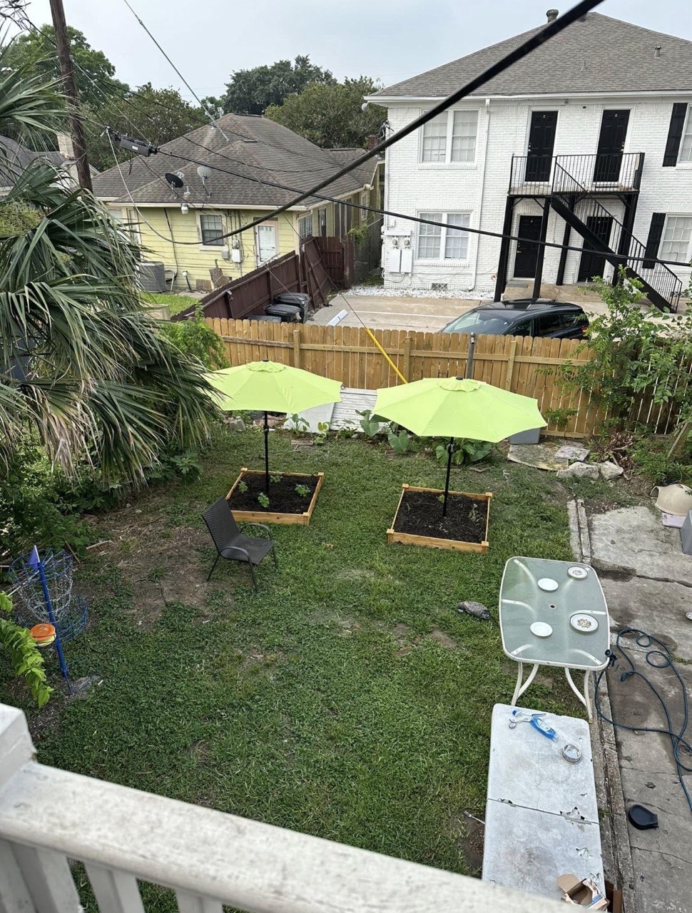 Two raised cedar flowerbeds with young plants, each shaded by a bright green patio umbrella, in the sanctuary yard